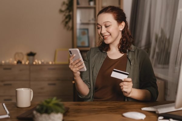 smiley-woman-using-her-smartphone-home-with-credit-card
